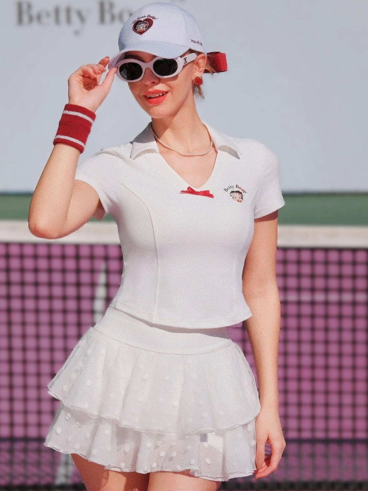 Woman in a white tennis outfit with a skirt and top, standing on a tennis court.