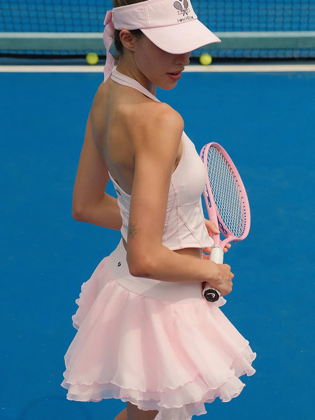 Woman in a white and pink tennis outfit holding a racket on a blue tennis court.