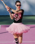 Model wearing macarons pink Betty Boop ruffle skirt on a tennis court, blending sporty and playful style.
