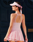 Woman wearing a pink tennis dress and visor against a dark background