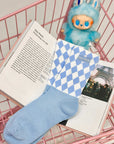 Sky blue mid-crew socks with checkered pattern and Pom Pêche logo, styled with a soft, casual aesthetic.