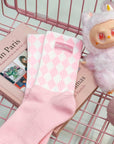 Pink mid-crew socks with checkered pattern and Pom Pêche logo, styled with a soft, casual aesthetic.