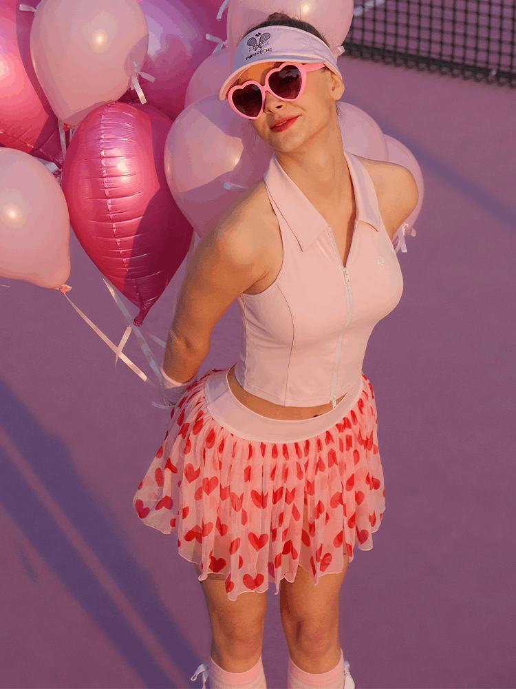 Mesh Tennis Skirt - Pink Heart styled with pink accessories, as the model poses with heart-shaped balloons on a pink tennis court
