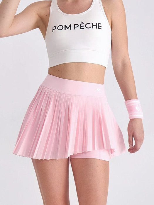 White pleated tennis skirt with red and blue stripes, styled with crop top and visor on a scenic bridge backdrop