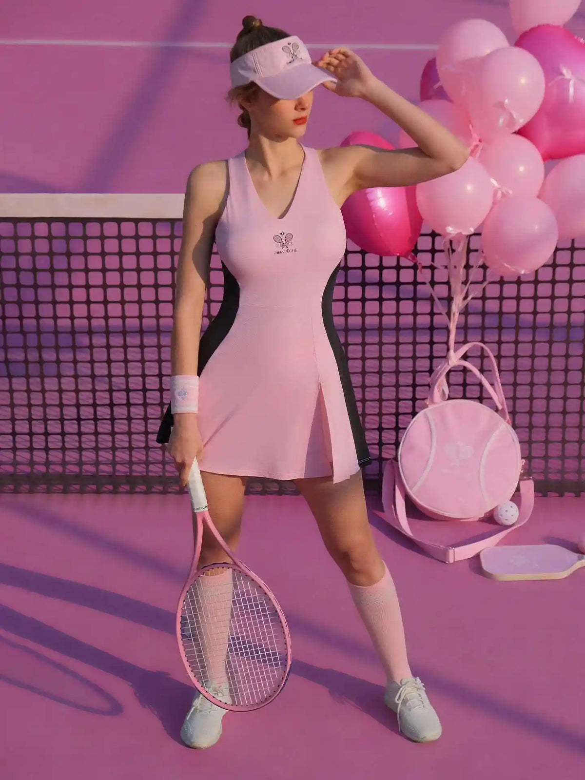 Pink V-neck tennis dress with black curved side panels, styled on the court.