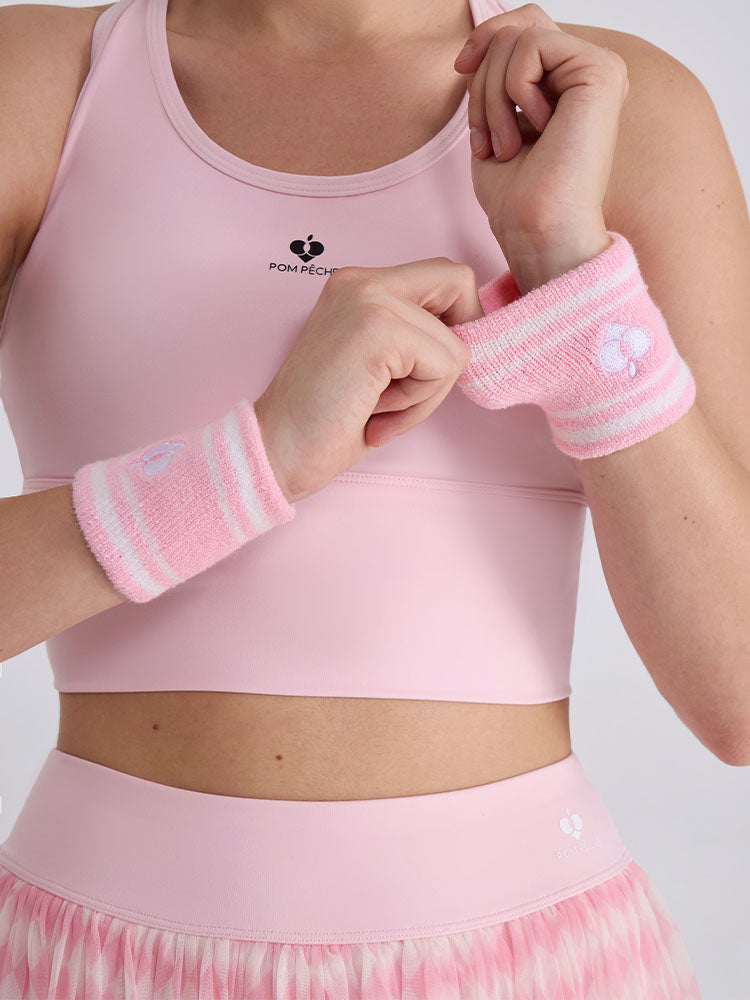 Soft pink tennis wristbands with white stripes, featuring logo details.