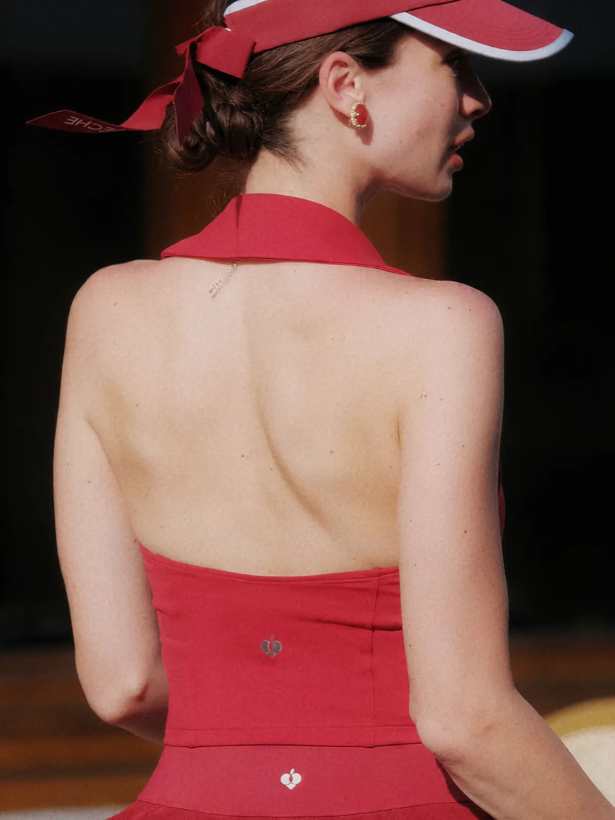 Woman wearing a red dress with a halter neck and visor in an indoor setting