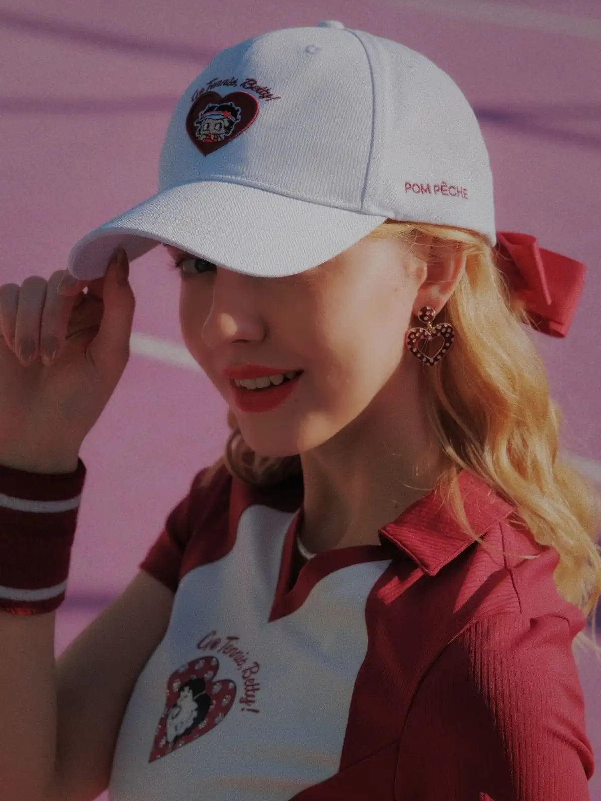 Person wearing a white cap with a heart design on a pink background