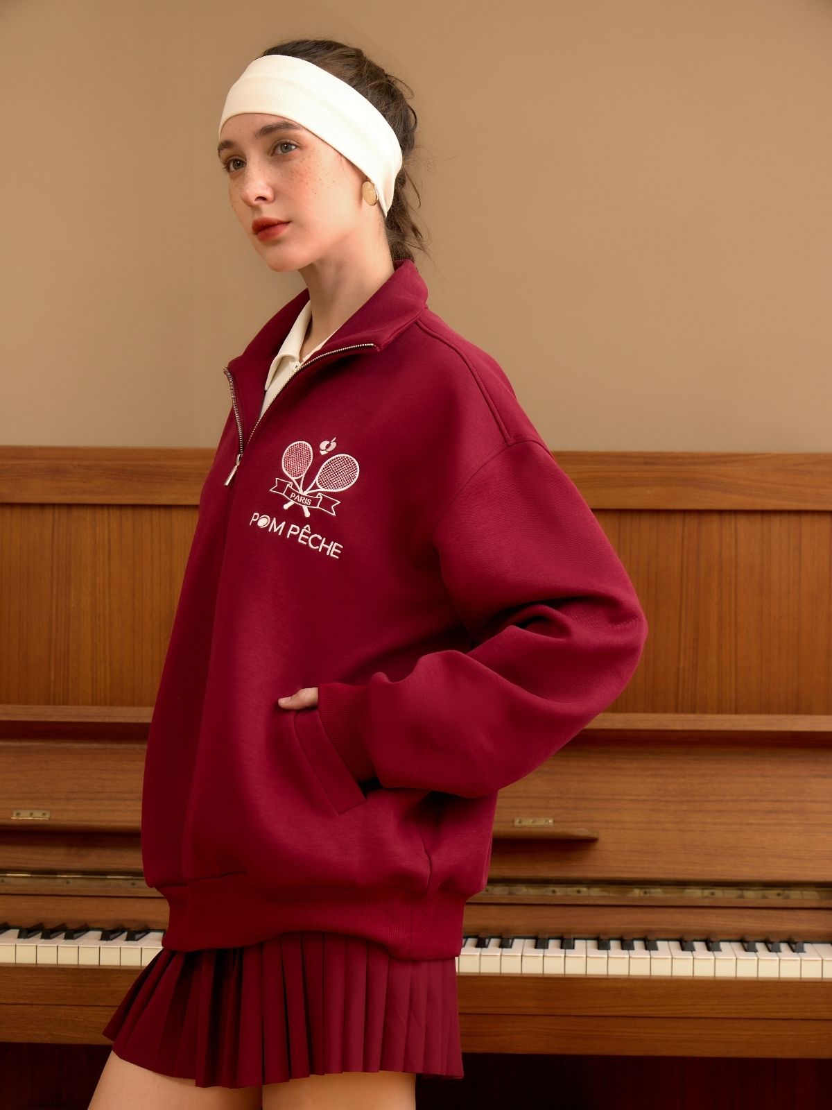 Woman wearing a maroon sweatshirt with a logo in front of a piano