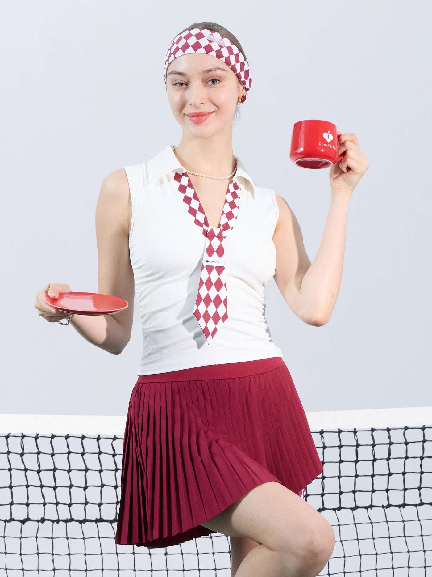 White slim-fit tennis top with a playful red diamond-pattern tie detail, styled for a chic on-court look.