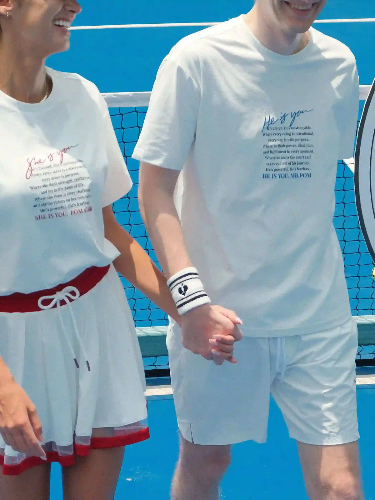 Two people on a tennis court wearing matching white outfits with text.