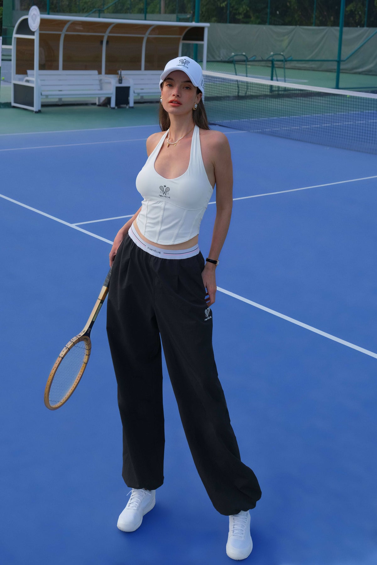 Classical white halter tennis top with a fitted silhouette and subtle logo detail, styled on the tennis court.