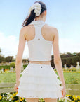 White cropped tennis top with ruffled collar and sleeveless design, featuring a subtle logo for a chic, sporty look.