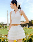 White cropped tennis top with ruffled collar and sleeveless design, featuring a subtle logo for a chic, sporty look.
