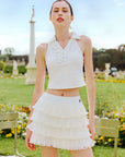 White cropped tennis top with ruffled collar and sleeveless design, featuring a subtle logo for a chic, sporty look.