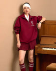 Person wearing a red outfit with a headband, standing next to a wooden piano against a beige wall.