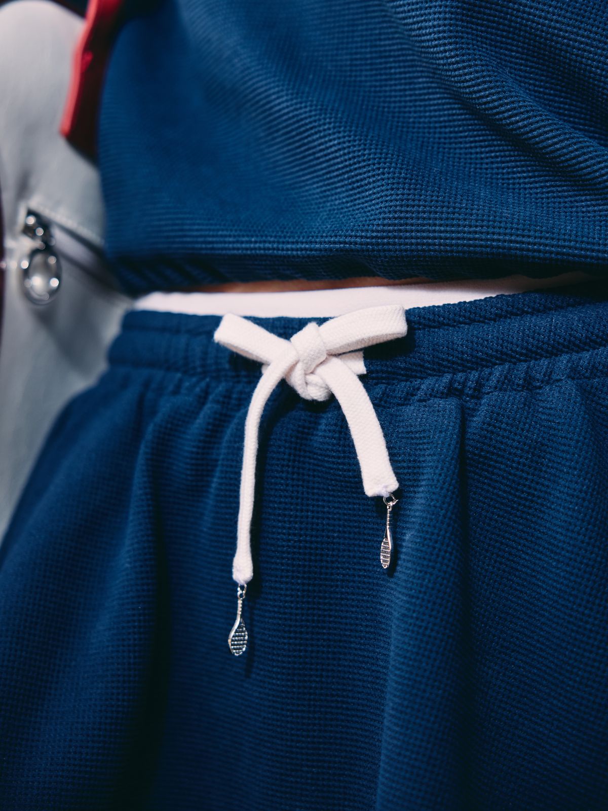 Close-up of navy tennis skirt waistband with white drawstring and custom tennis racket pendants.
