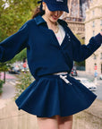 Woman wearing navy A-line tennis skirt and long-sleeve top, posing outdoors near the Eiffel Tower.