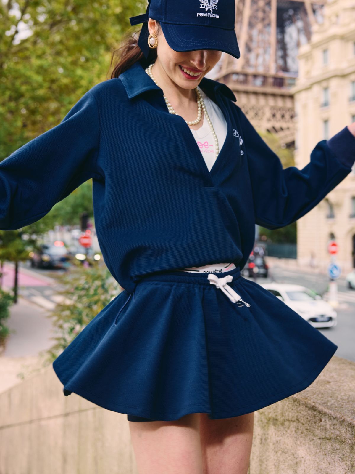 Woman wearing navy A-line tennis skirt and long-sleeve top, posing outdoors near the Eiffel Tower.