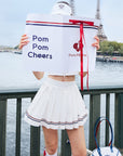 Person holding a 'Pom Pom Cheers' sign with the Eiffel Tower in the background