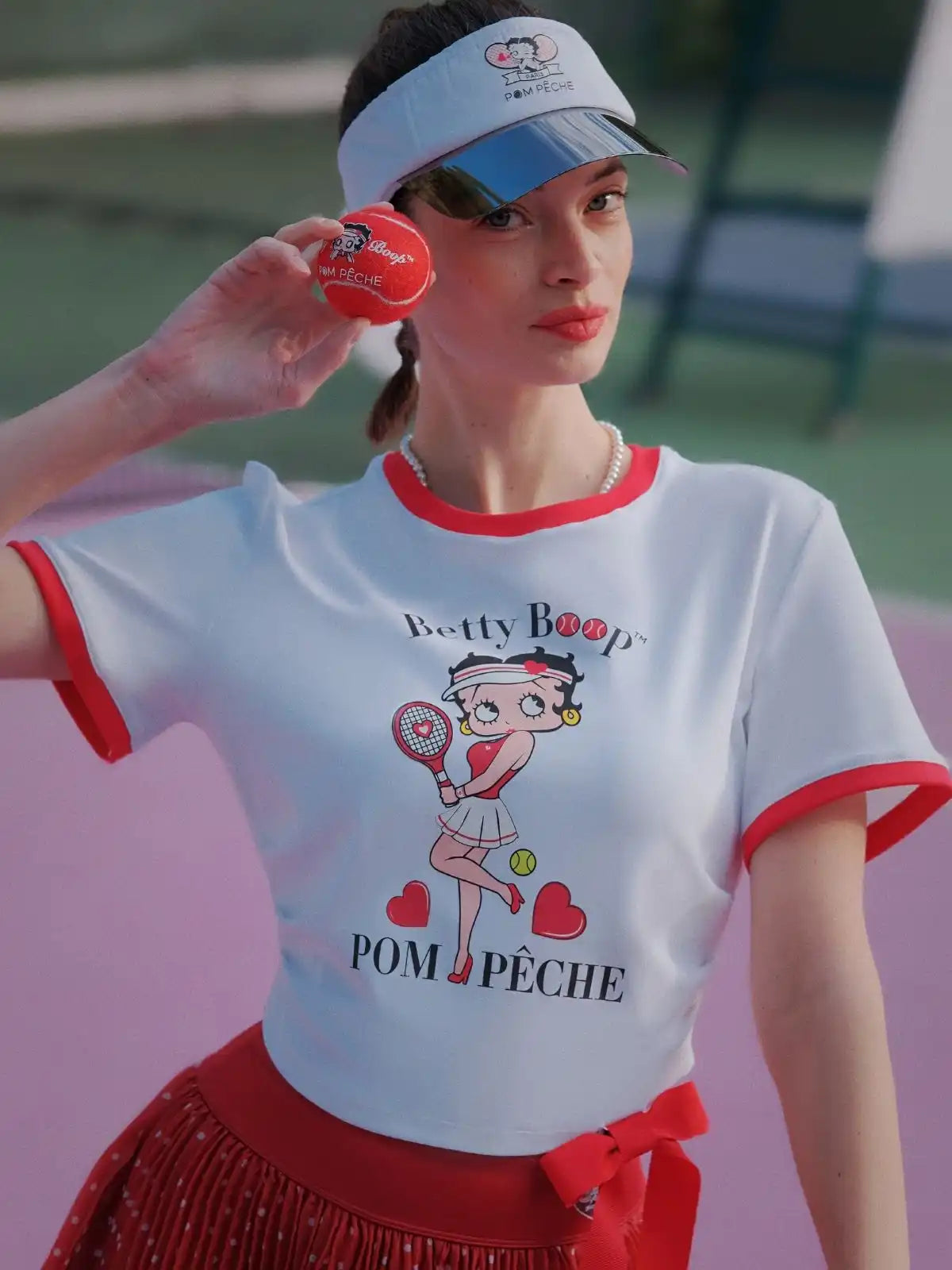 Person wearing a Betty Boop-themed shirt and visor on a tennis court