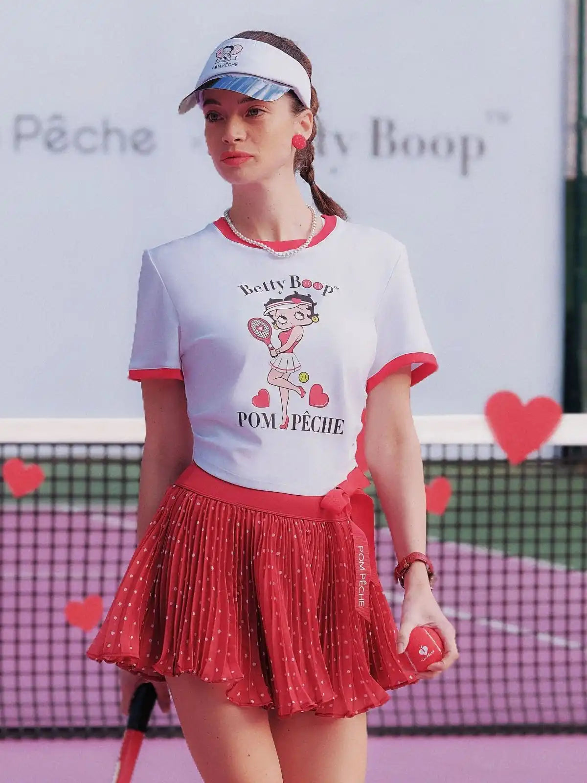 Person wearing a Betty Boop-themed shirt and visor on a tennis court