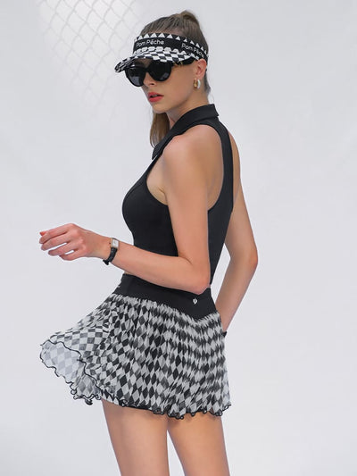A woman walks in front of a white backdrop wearing a black and white argyle mesh tennis skirt and black athletic top.
