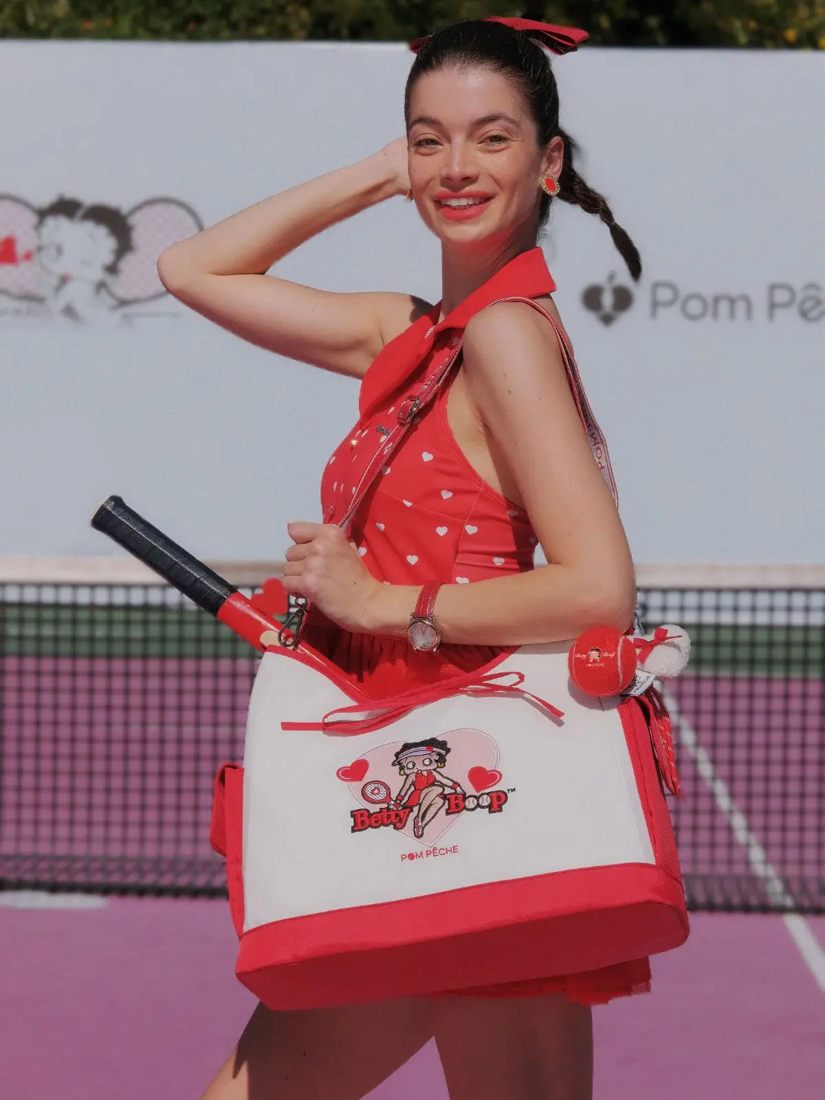 Woman in a red dress holding a Betty Boop bag on a tennis court
