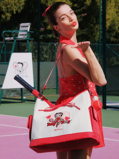 Woman in a red dress with a Betty Boop bag on a tennis court