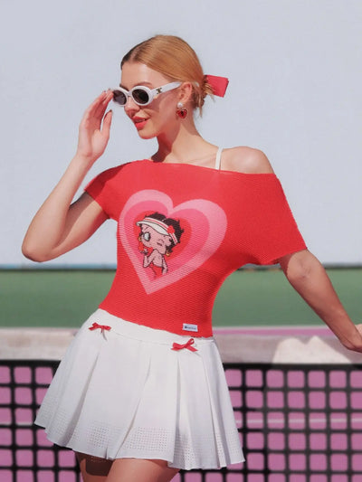Woman wearing a red off-shoulder top with a heart design and white skirt on a tennis court.