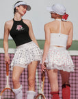 Two women on a tennis court wearing vintage-style tennis outfits.