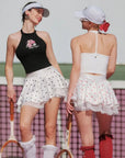 Black halter top with graphic design worn by a person, with a blurred background.
