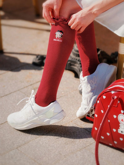 Person wearing red leggings with a logo and white sneakers, standing next to a red bag with white polka dots.