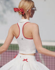 Woman wearing a white outfit with red accents, standing outdoors.