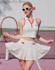 Woman in a white tennis outfit with red accents on a tennis court.