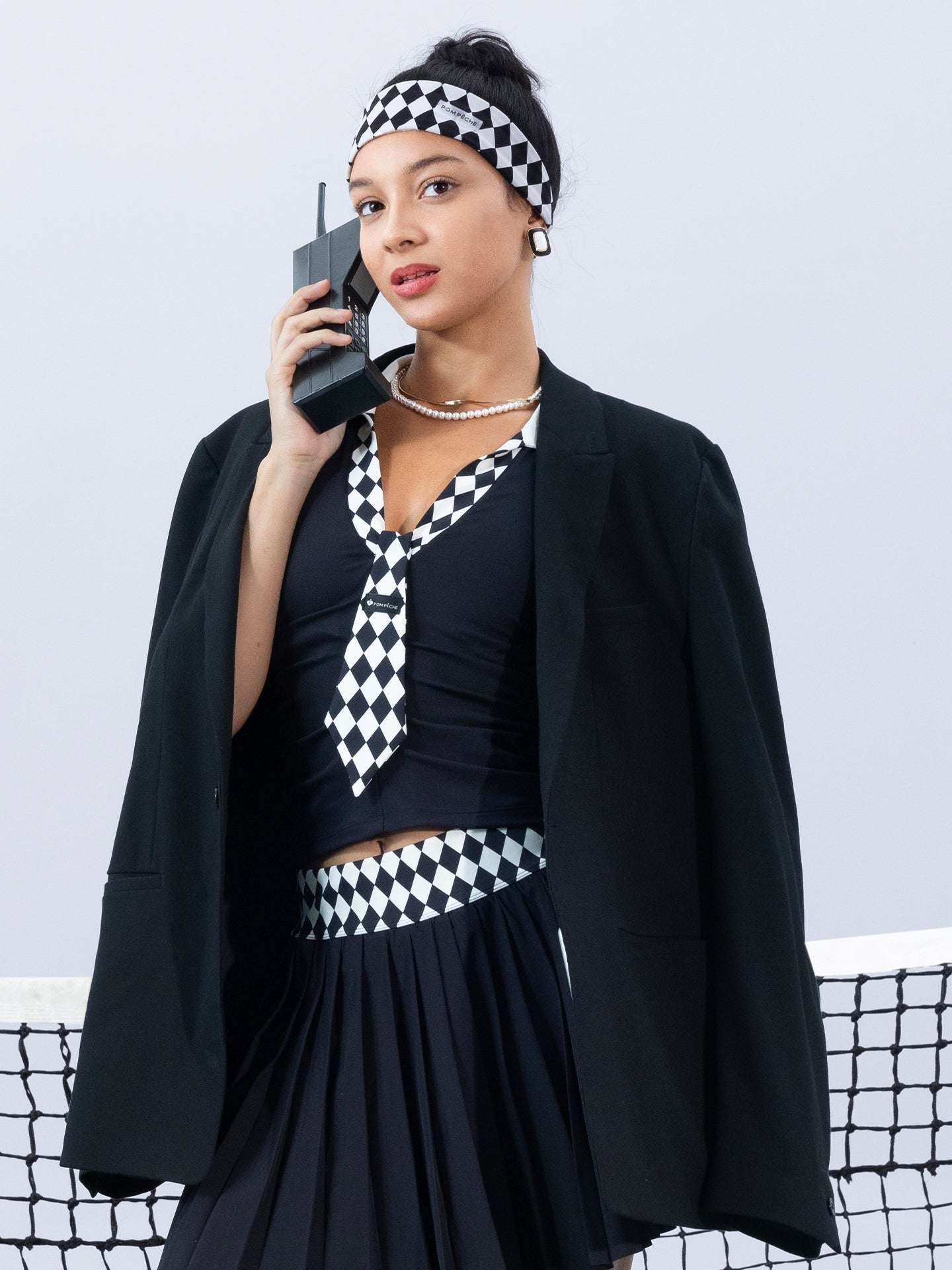 Black slim-fit tennis top with a playful diamond-pattern tie detail, styled for a chic on-court look.