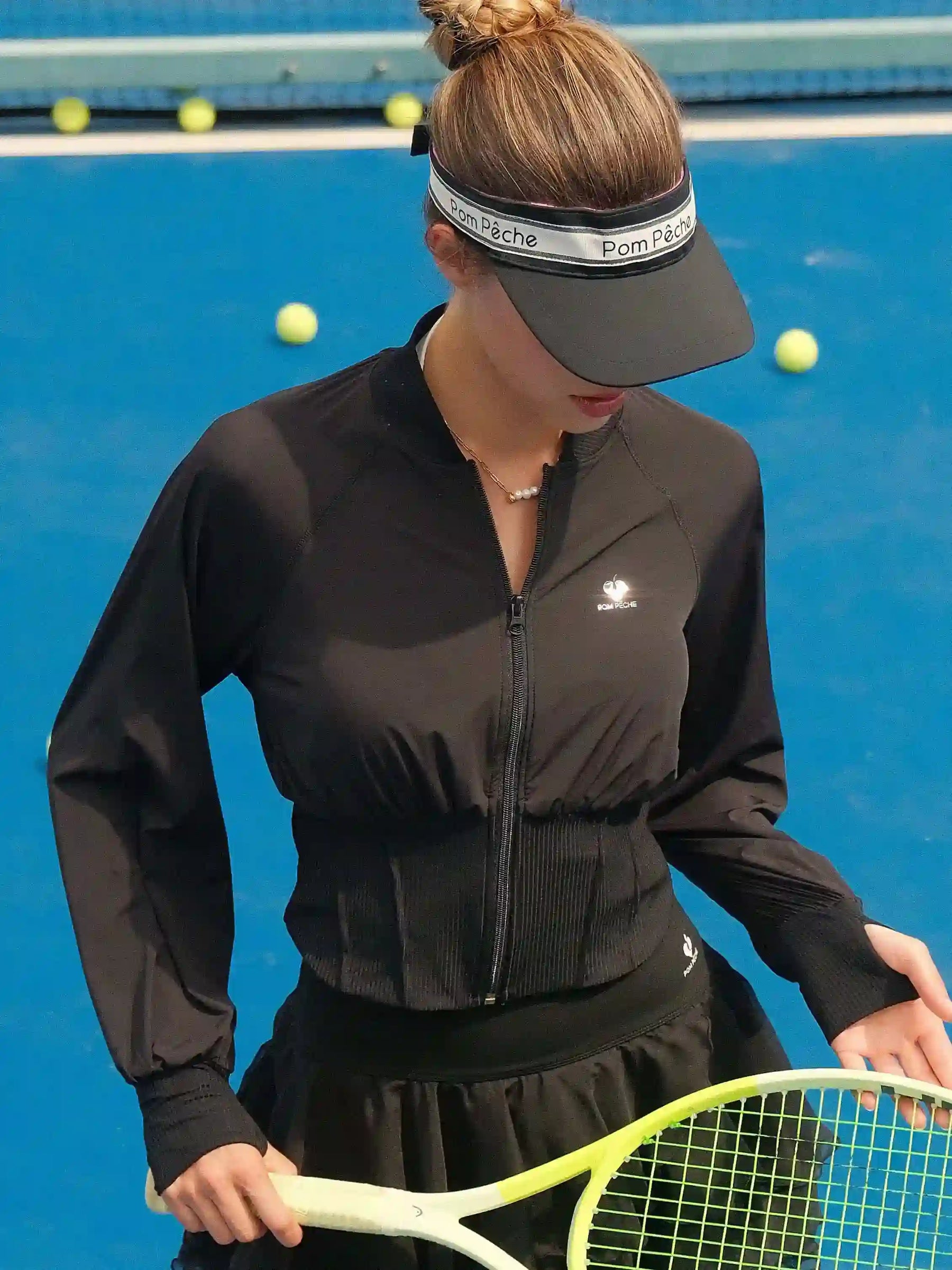 Person on a tennis court wearing a black outfit and visor, holding a tennis racket.