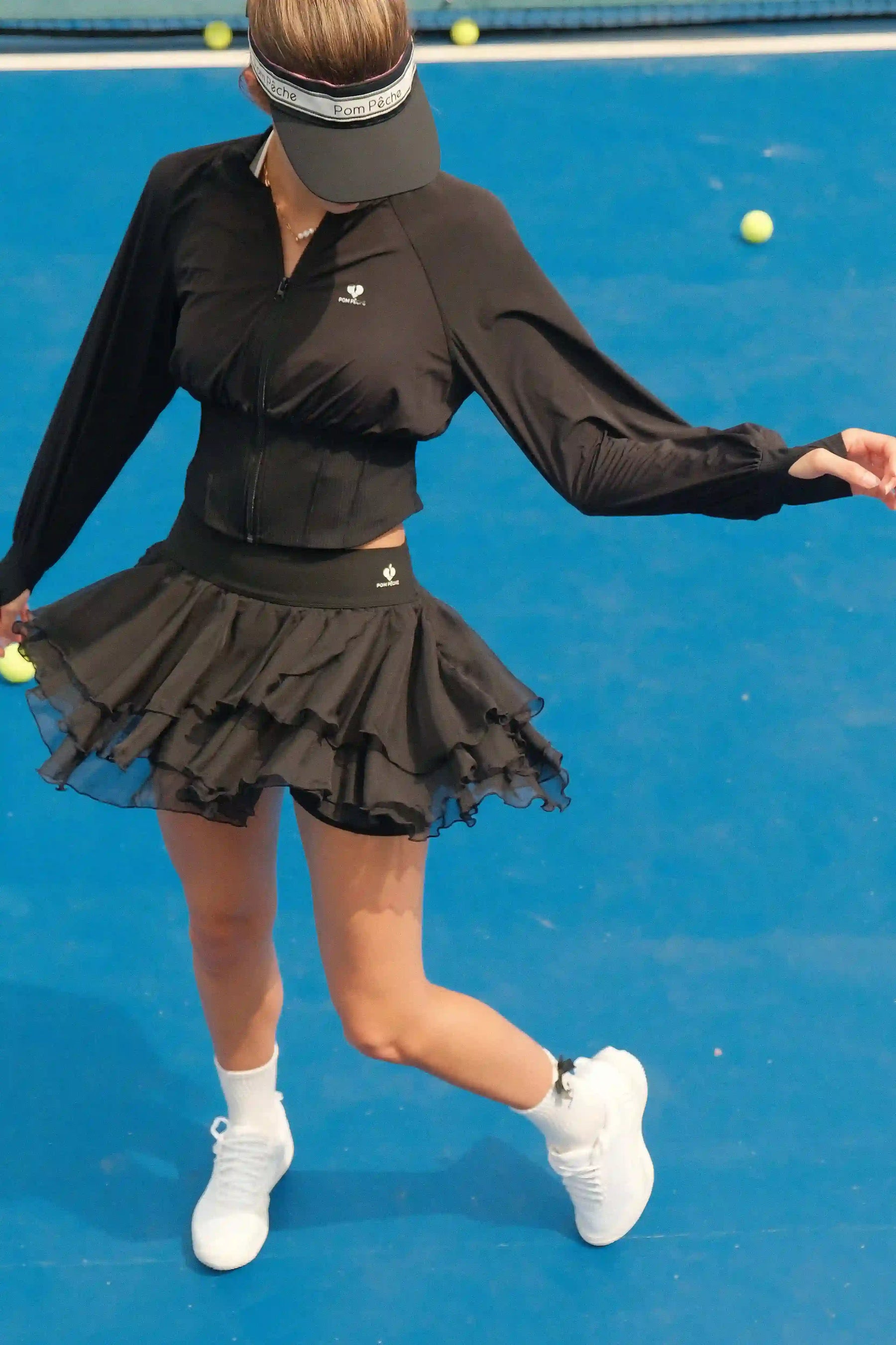 Person in black tennis outfit on a blue court with tennis balls.