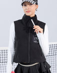 Warm black fleece vest with high-neck zip design and embroidered chest pocket, styled on the tennis court.