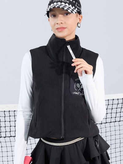 Warm black fleece vest with high-neck zip design and embroidered chest pocket, styled on the tennis court.