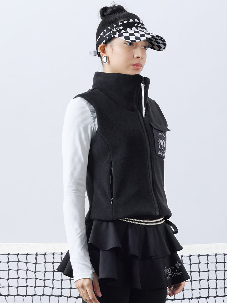 Warm black fleece vest with high-neck zip design and embroidered chest pocket, styled on the tennis court.