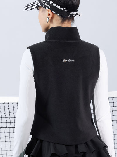 Warm black fleece vest with high-neck zip design and embroidered chest pocket, styled on the tennis court.