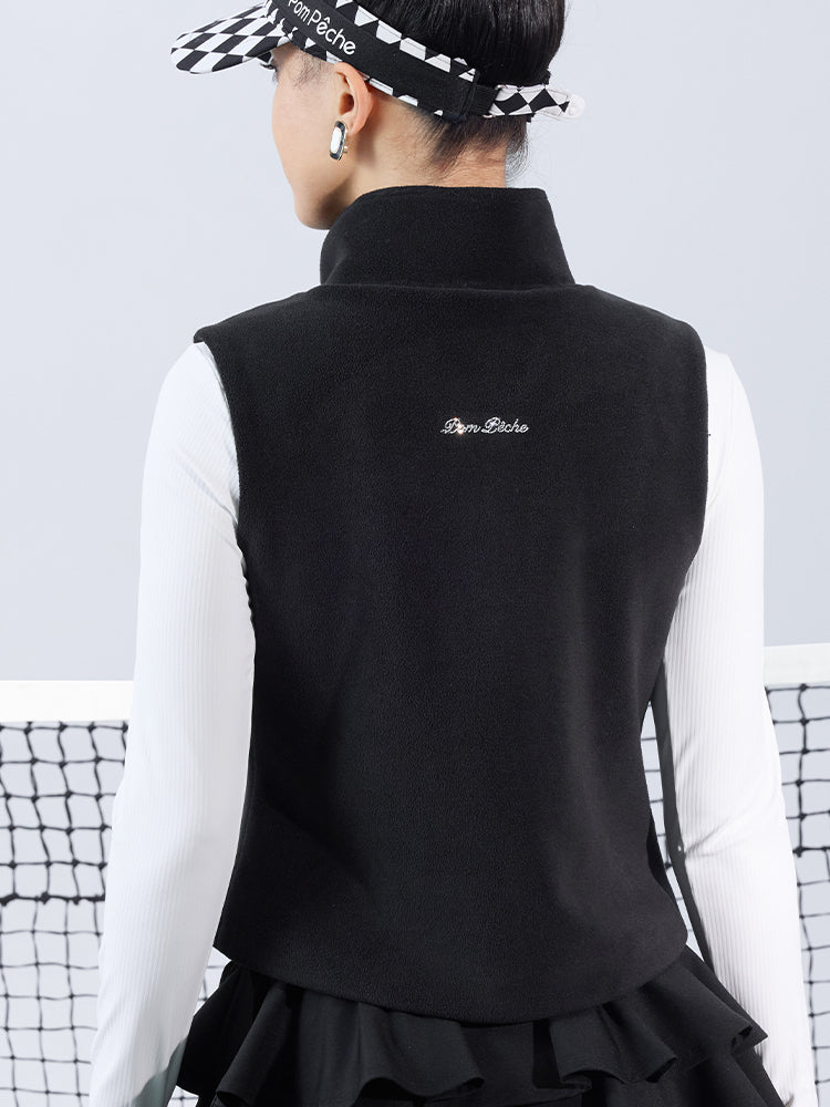 Warm black fleece vest with high-neck zip design and embroidered chest pocket, styled on the tennis court.