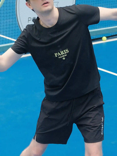 Person wearing a black 'Paris' branded outfit on a blue tennis court.