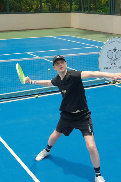 Person playing tennis on a blue court with a racket and ball.