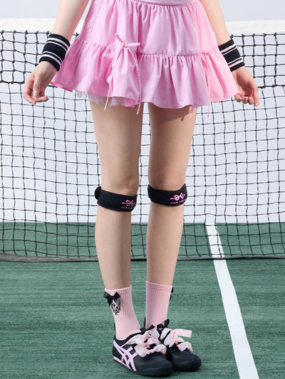 Tennis look featuring a black patella support strap with bow print. 