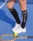 Black knee-high tennis socks with classical white stripes, bow detail, and logo embroidery.