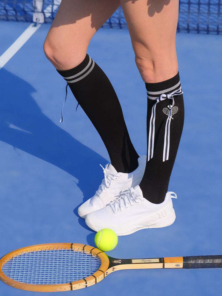 Black knee-high tennis socks with classical white stripes, bow detail, and logo embroidery.