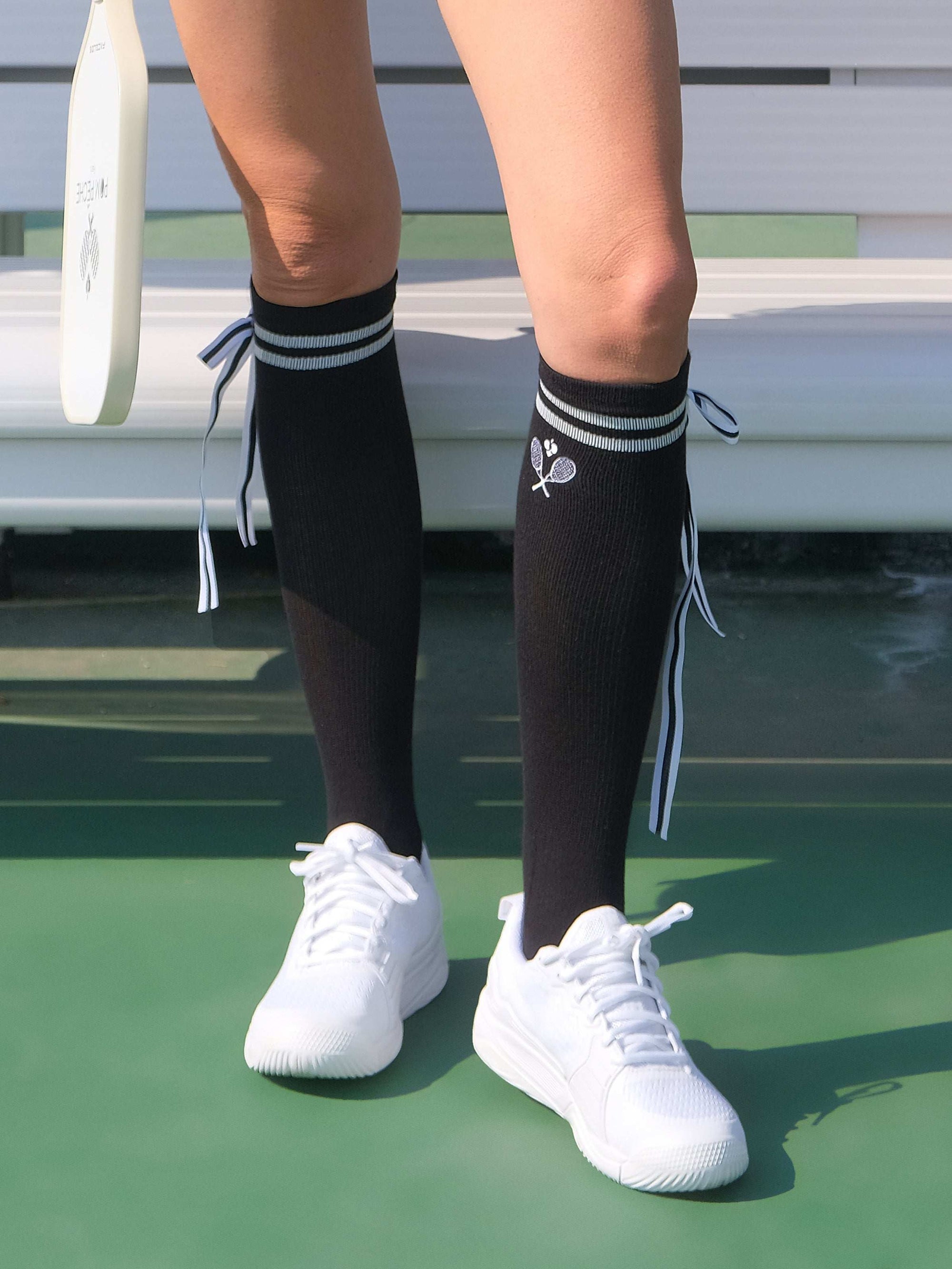 Black knee-high tennis socks with classical white stripes, bow detail, and logo embroidery.