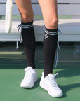 Black knee-high tennis socks with classical white stripes, bow detail, and logo embroidery.